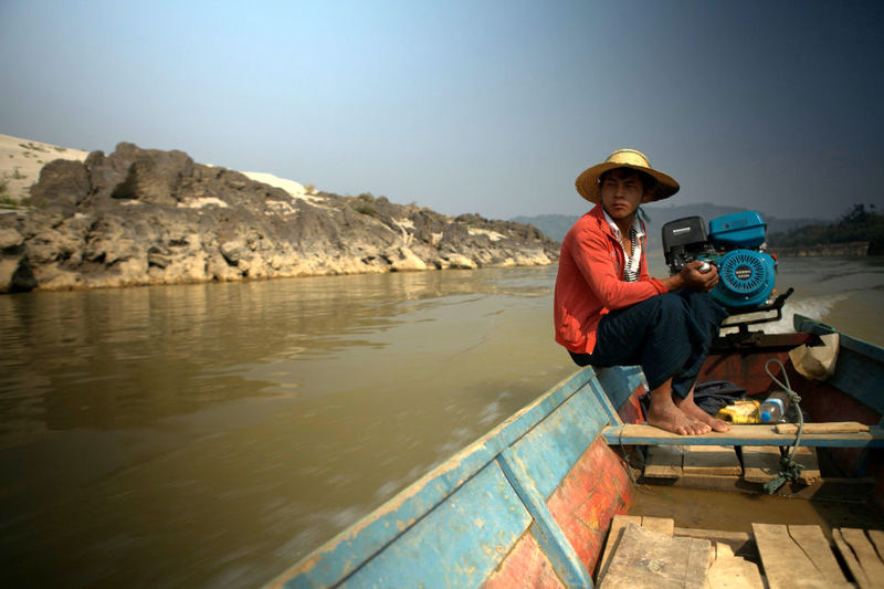 A young fisherman steers his boat on the Irrawaddy River towards the dam construction site
