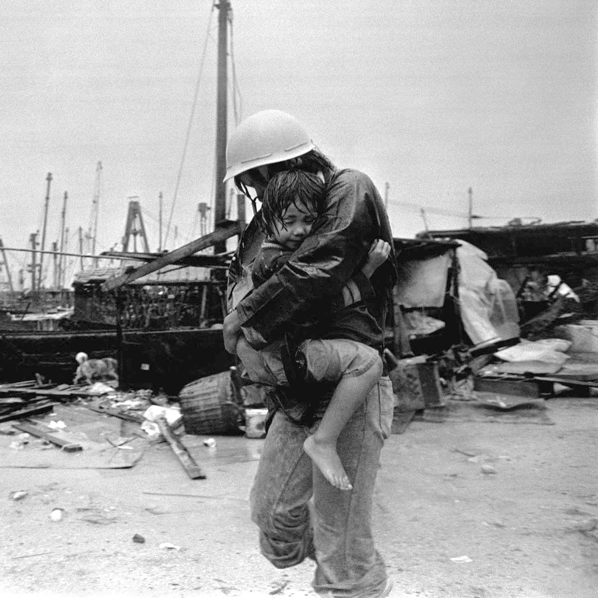 A rescuer carries a young survivor past the debris left behind by Typhoon Hope