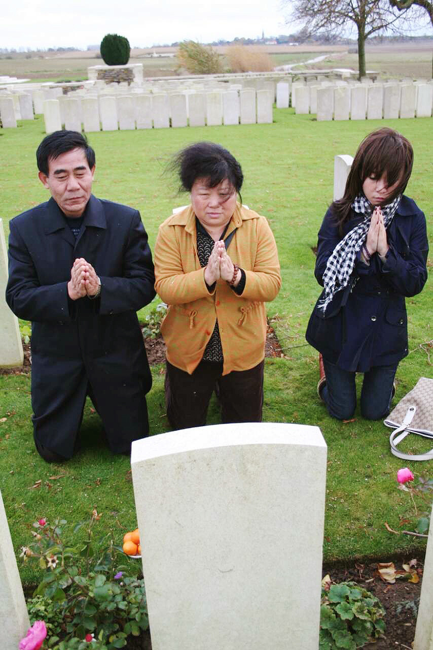 Cheng Ling kneels along with her husband and daughter at her grandfather's grave in France